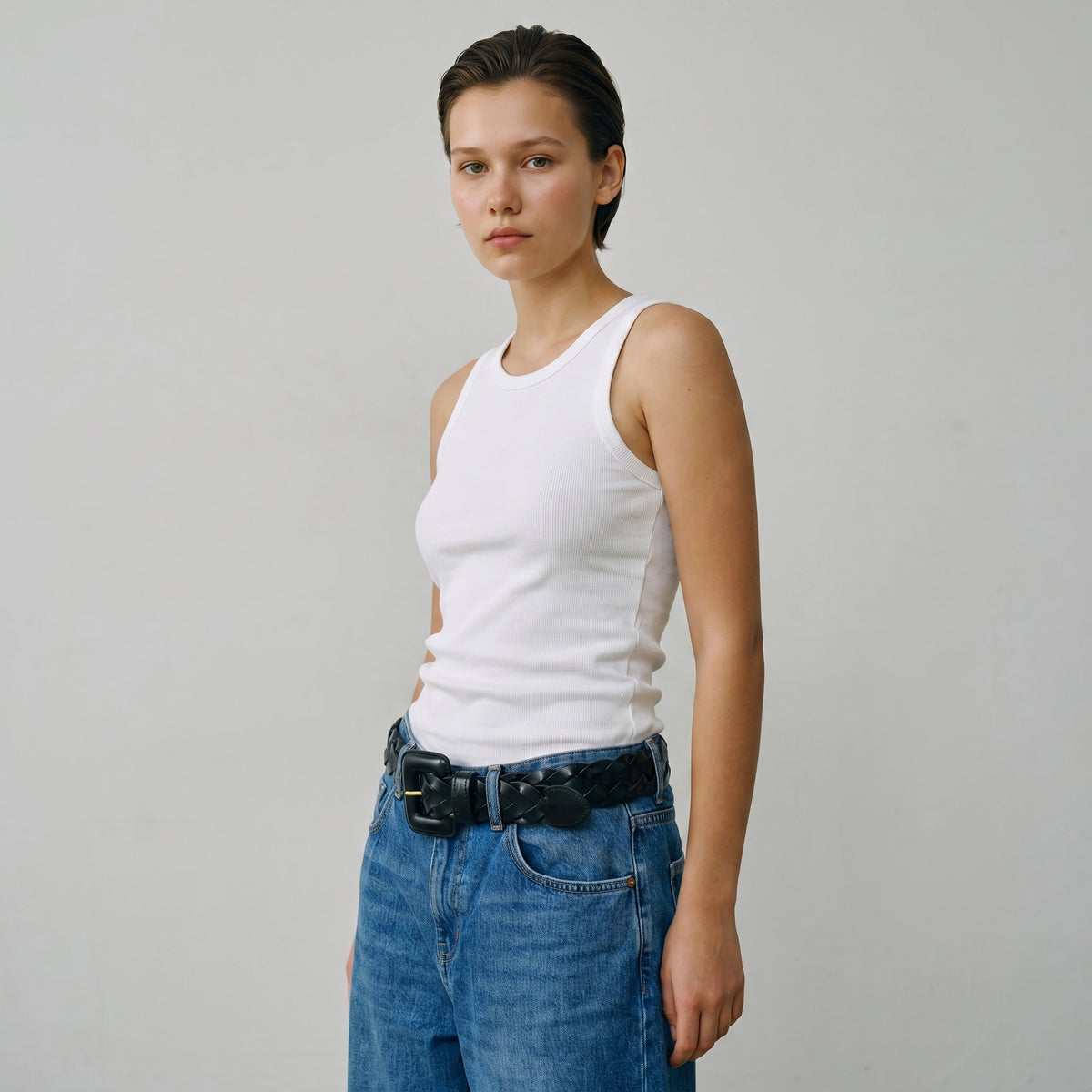 Modèle portant une ceinture tressée en cuir noir La Stella avec une boucle géométrique sur un jean bleu